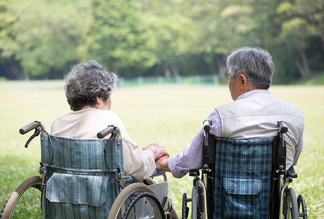 An elderly couple with dementia in wheelchairs taking time to enjoy the park.