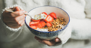 A young woman holding a bowl of granola and strawberies with yoghurt for breakfast