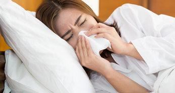 Woman lying in bed and blowing her nose due to a flu