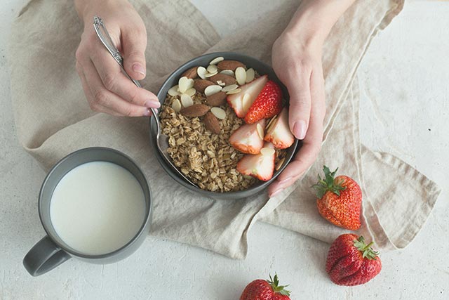 A lady cradling a bowl of cereal with fresh strawberries and almonds