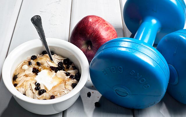 Bowl of yoghurt with honey, nuts, and raisins beside a dumbbell and an apple