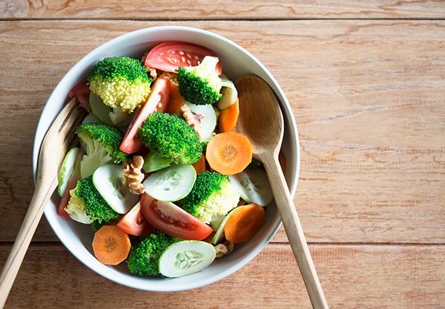 A bowl of brocolli, tomatoes, cucumbers and carrots sliced thinly and tossed together