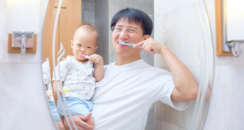 Asian fathers brushing teetch with his son in arms